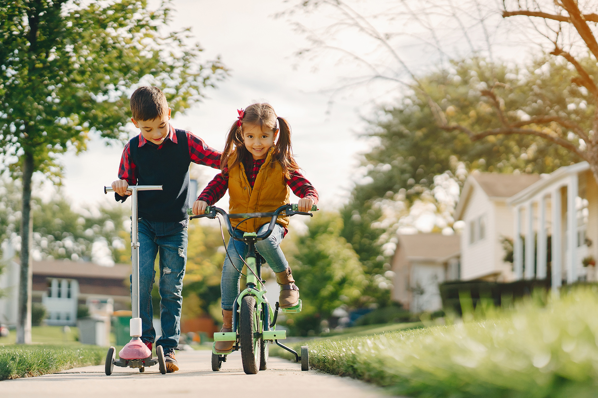 Brother and sister in a park. Boy with scooter. Girl with bicycle.